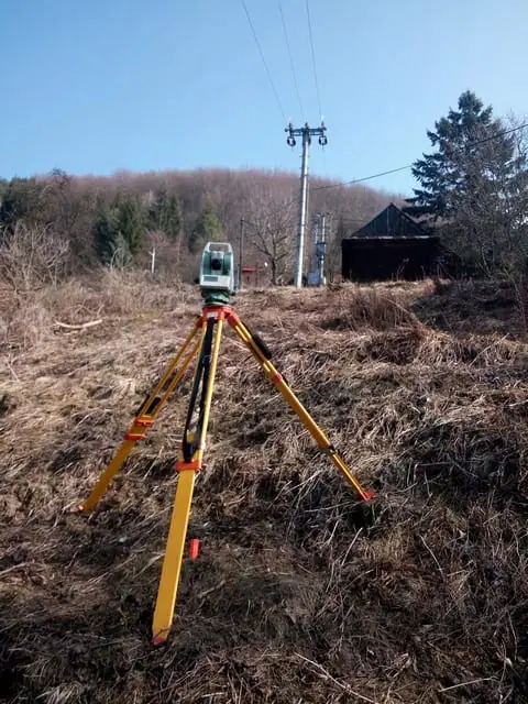 Totálna stanica na lúke pred stĺpom elektrického vedenia