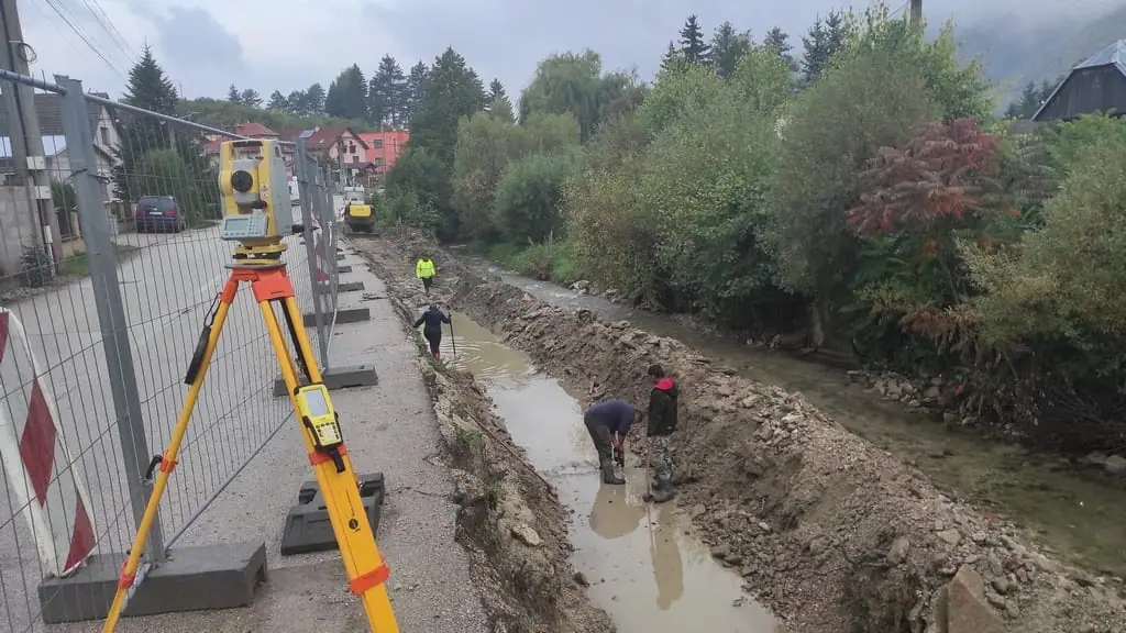Totálna stanica pri výkope pozdĺž potoka a cesty