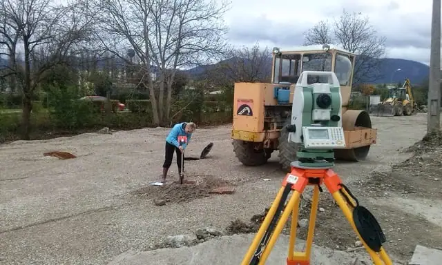 Totálna stanica na stavbe kanalizácie, v pozadí valec a pracovníčka so sprejom