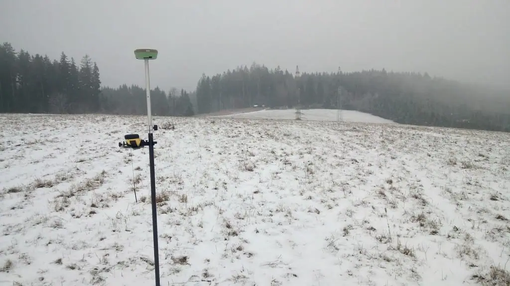 GNSS prijímač na výtyčke na zasneženej lúke pri lese v hmle