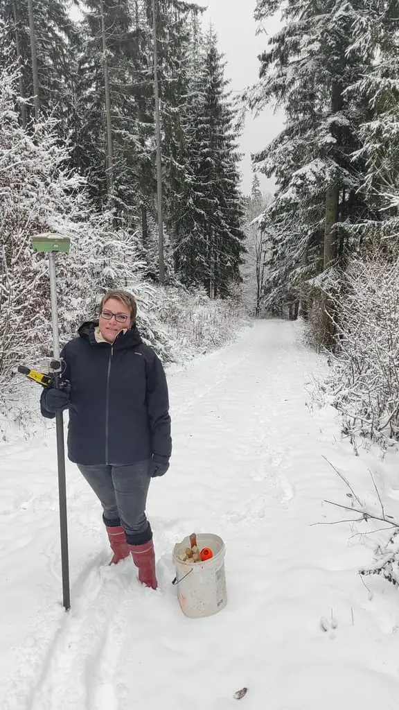 Geodetka s GNSS prijímačom na výtyčke v zasneženom lese