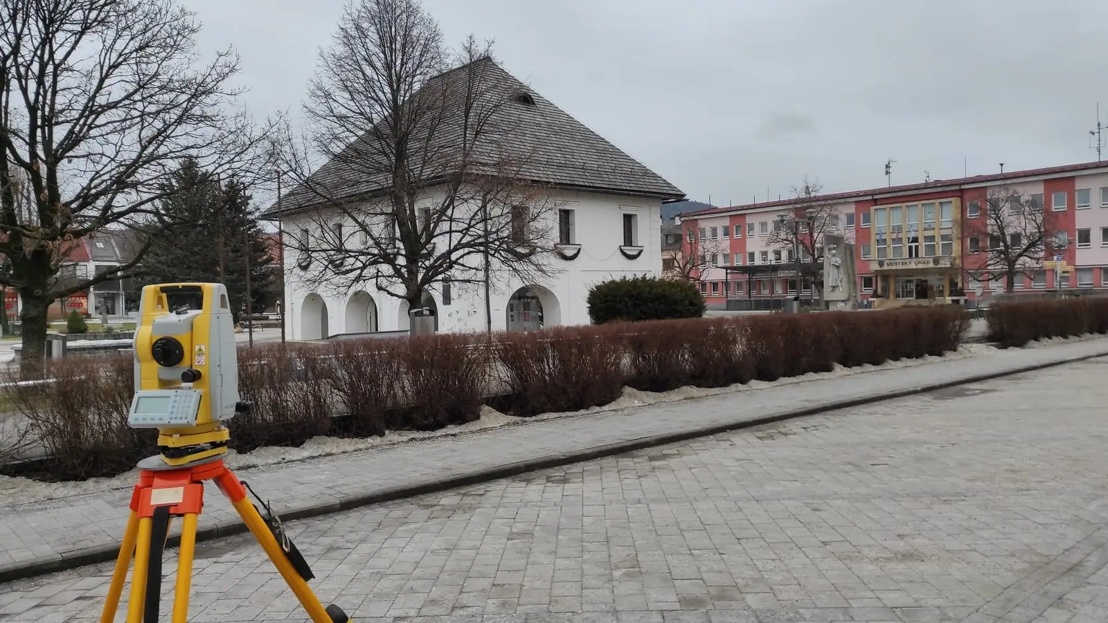 Totálna stanica na statíve na námestí s historickou budovou v pozadí