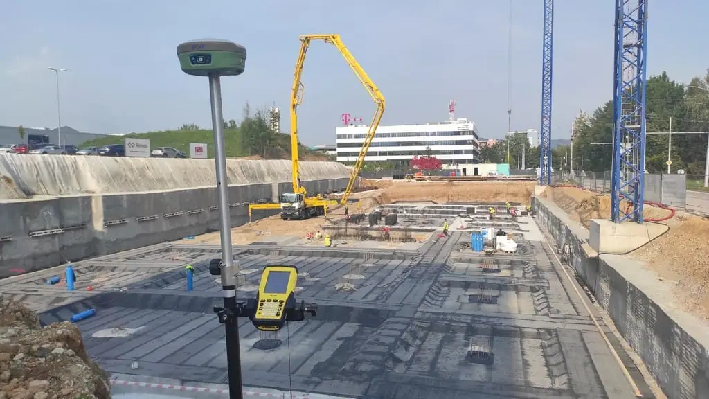 GNSS prijímač na výtyčke pri betónovej základovej doske na stavenisku