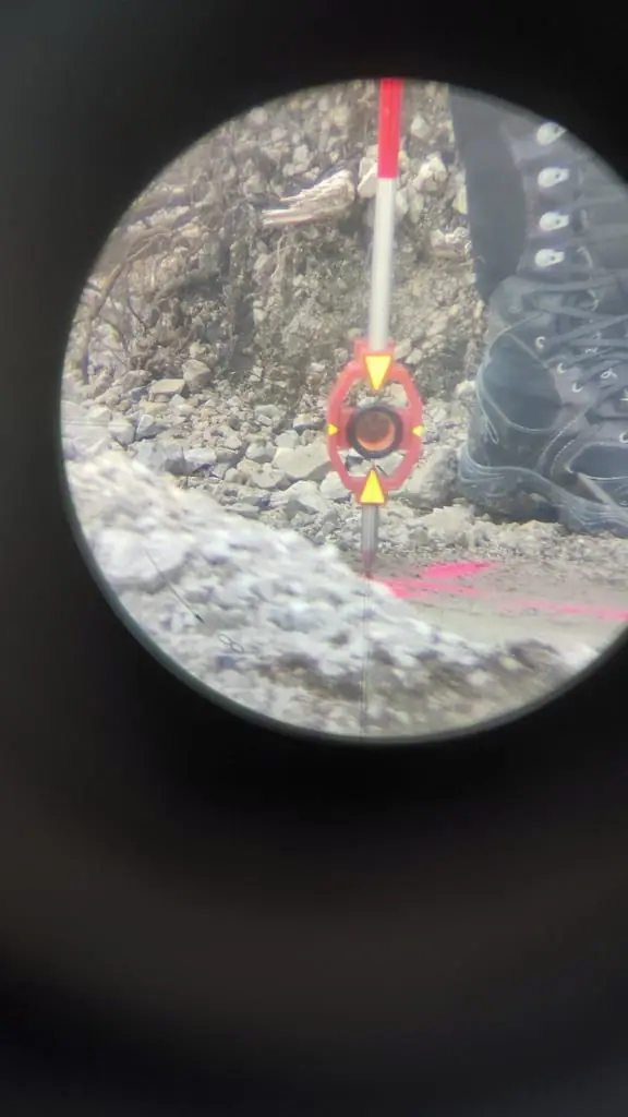 Pohľad cez ďalekohľad totálnej stanice na hranol na výtyčke