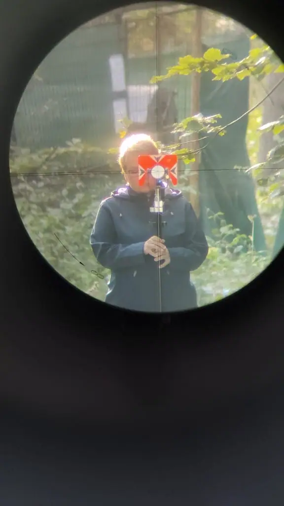 Pohľad cez ďalekohľad totálnej stanice na geodetku s hranolom v lese